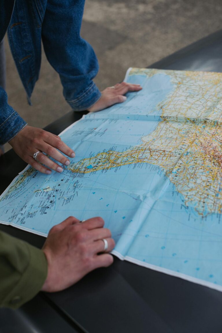 Hands of a young couple planning a road trip using a large map outdoors.