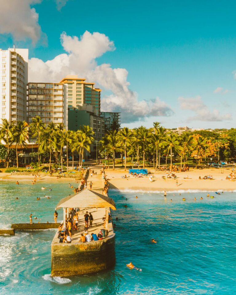 Vibrant tropical beach scene with a bustling pier, palm trees, and resort buildings.